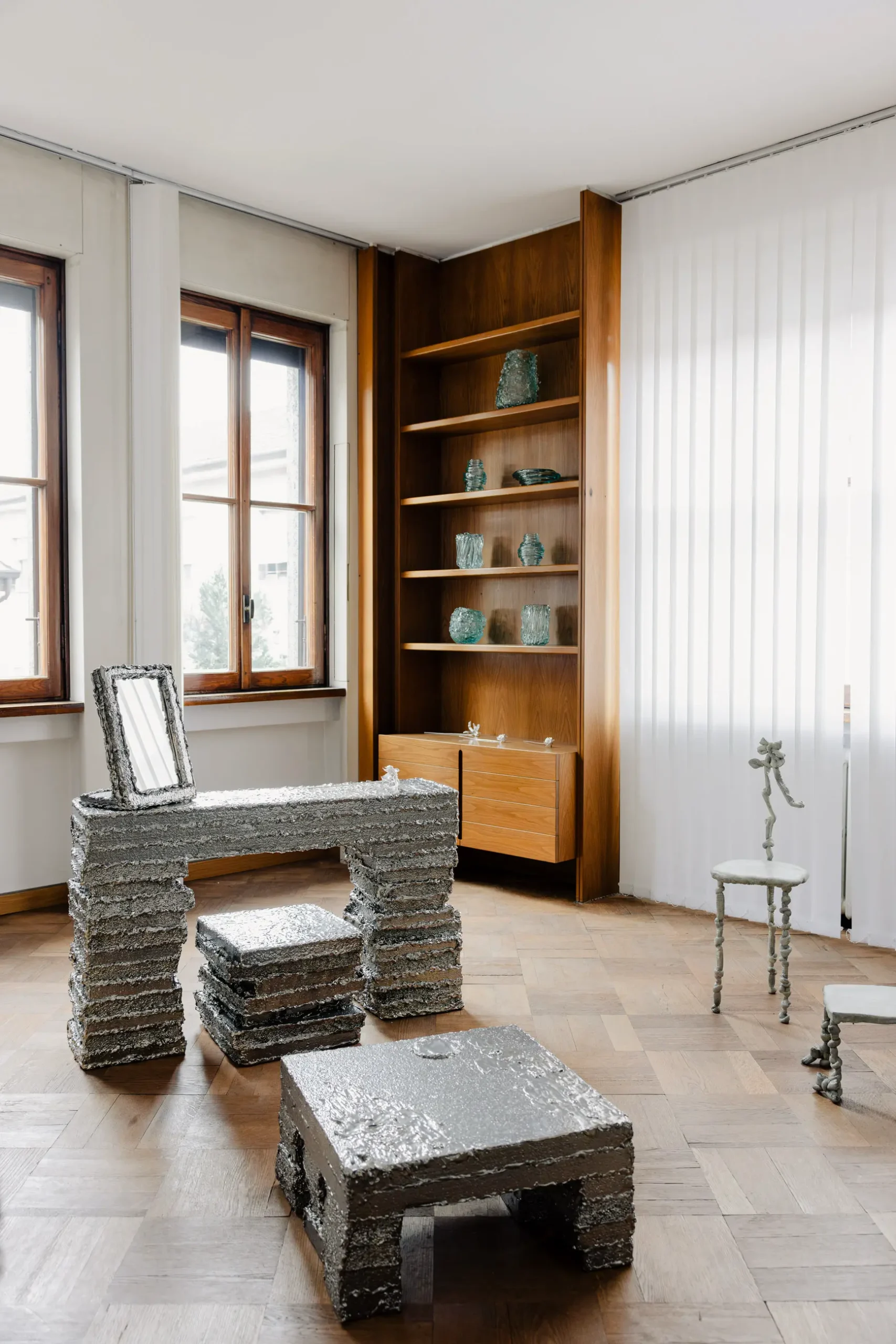 Atmospheric contemporary design installation at Alcova Milan with experimental interiors, sculptural objects, raw textures, and dramatic architectural light.